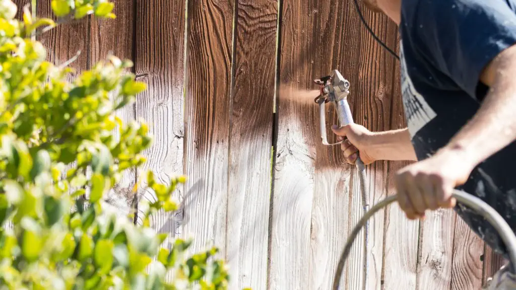 Here's a person staining a fence with high pressure